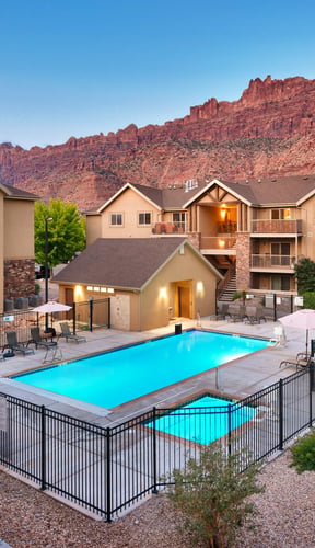 Resort pool and buildings beneath dramatic Moab red rock cliffs at dusk