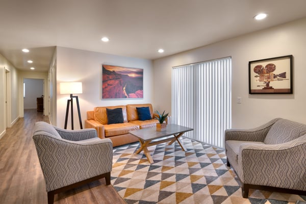 Modern living room with orange leather sofa, patterned armchairs, geometric area rug, and framed artwork on walls